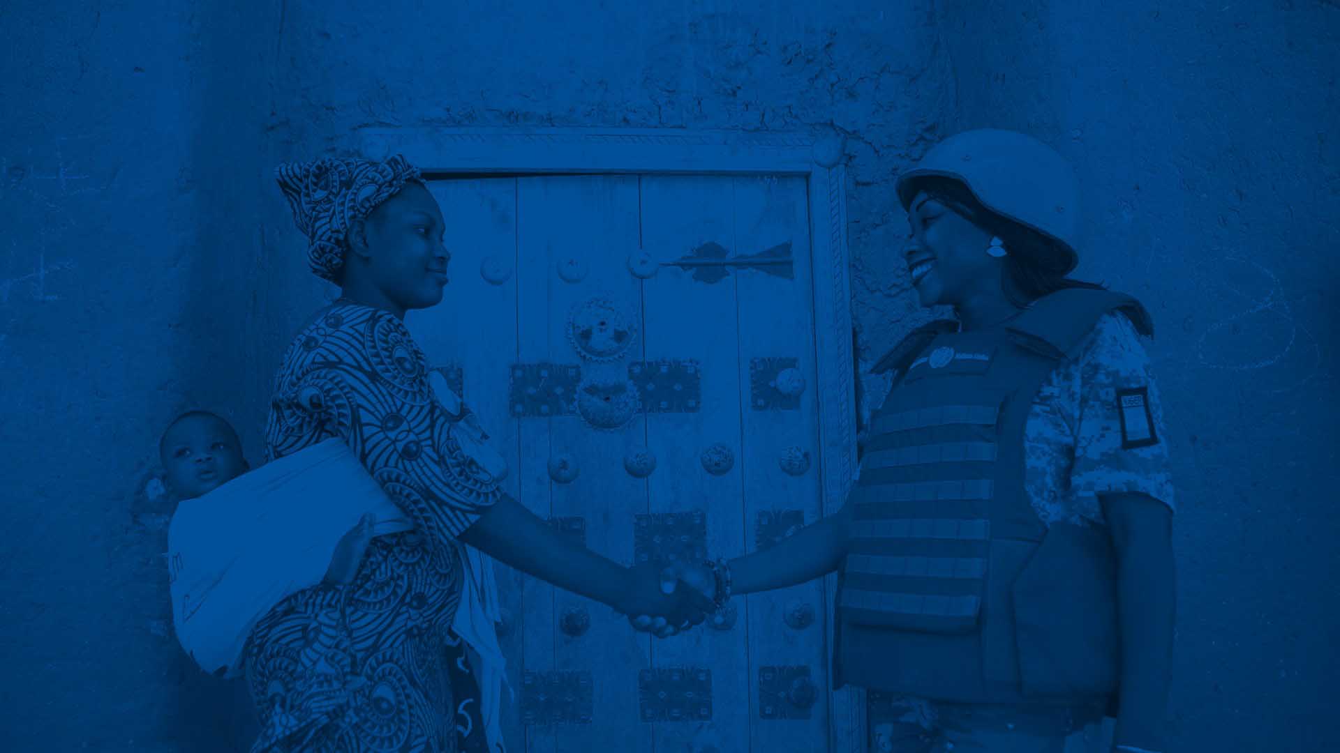 A woman carrying a baby on her back shakes hands with a female UN peacekeeper