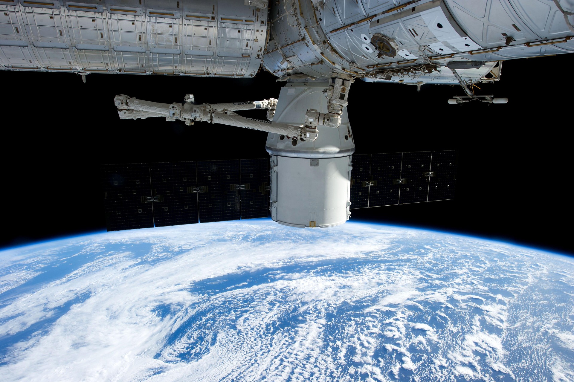 A spacecraft capsule docked to a space station in orbit above Earth’s curved horizon, illustrating the growing presence of infrastructure in orbit and the governance questions it raises.