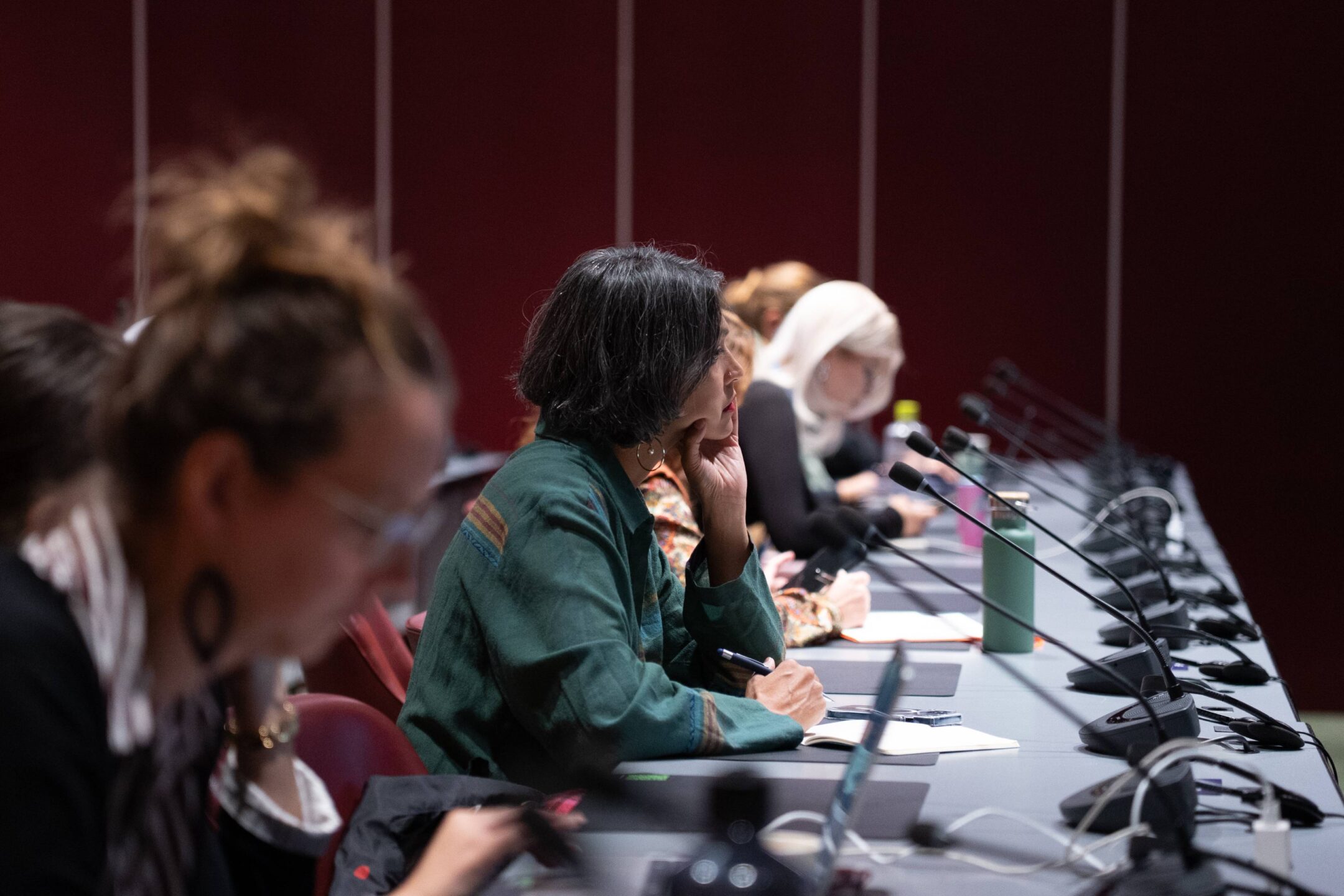 A participant rests her chin on her hand while listening and taking notes at a row of desks with microphones, during the launch of the Lomé Initiative’s third phase at the Geneva Peace Forum.