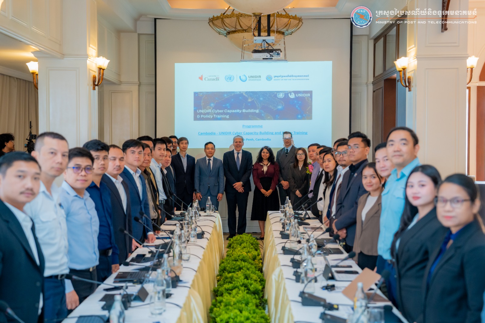 Participants stand along two conference tables at the Cambodia–UNIDIR Cyber Capacity-Building and Policy Training in Phnom Penh, with the programme displayed on screen.