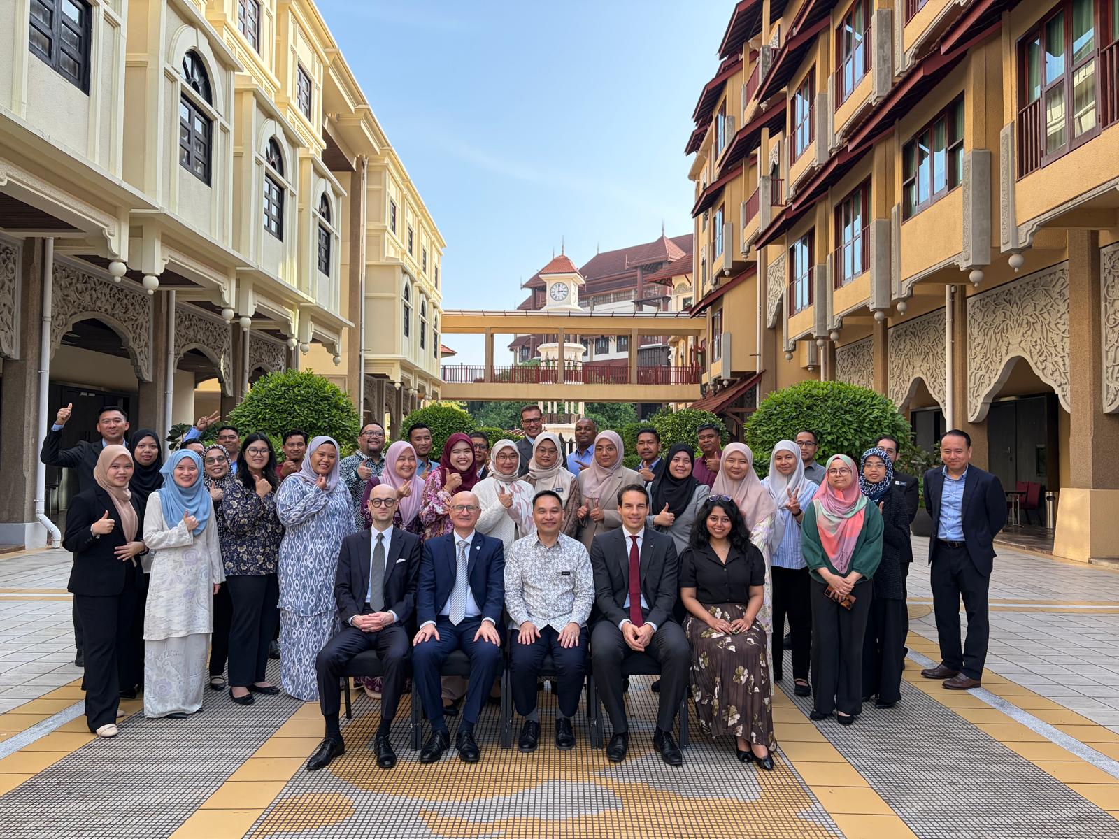 Participants in a UNIDIR cyber capacity-building training in Malaysia pose for a group photo in an outdoor courtyard, several giving a thumbs-up.