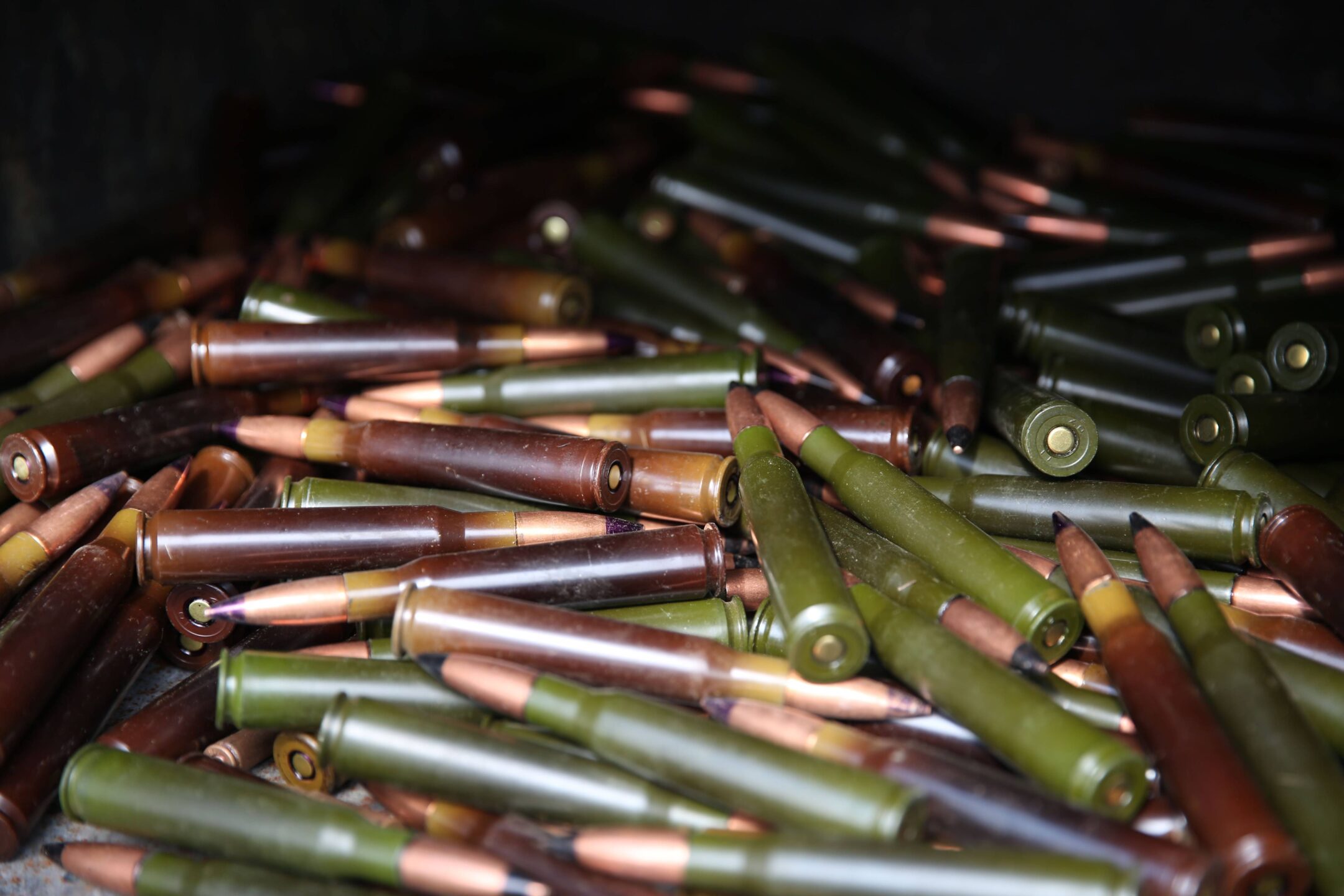 Close-up of small arms ammunition cartridges with green and brown casings piled in an incinerator, ready for destruction.