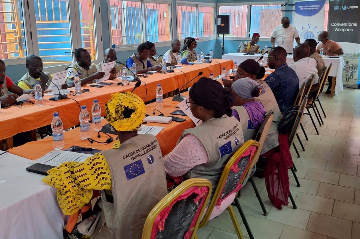 Community early-warning monitors seated at long tables reviewing training materials during the UNIDIR and WANEP workshop on ammunition diversion and trafficking in Ouangolodougou, Côte d’Ivoire.